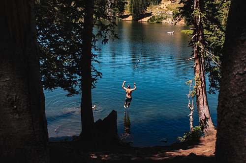 tree man jump into river at daytime lake